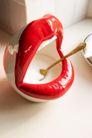 A close up image of a salt pig shaped like an open mouth with red lips placed on a white kitchen surface. 