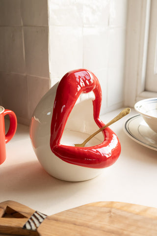 A lifestyle image of a salt pig shaped like an open mouth with red lips placed on a white kitchen surface. 