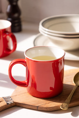 Red ceramic mug styled on a wooden chopping board with white cereal bowls in the background 