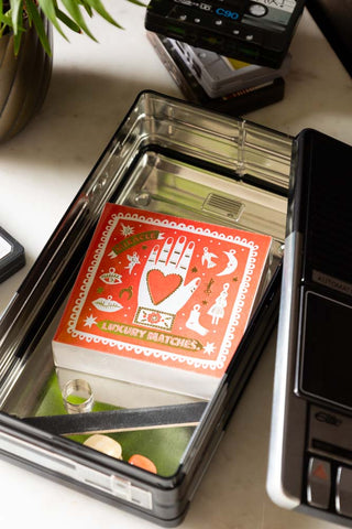 Close-up of the Retro Cassette Recorder Storage Tin with the lid off, styled with some matches and other accessories inside, displayed with a potted plant and some cassette tape storage tins.