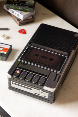 The Retro Cassette Recorder Storage Tin with the lid on, styled on a white surface with various small accessories and cassette tape storage tins. 