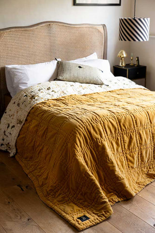 The Reversible Gold Rock & Rose Throw styled on a rattan bed.