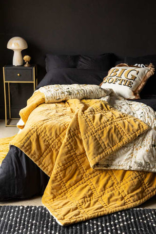 The Reversible Gold Rock & Rose Throw styled on a bed in a dark room.