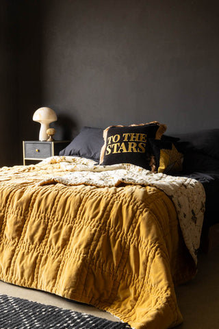 The Reversible Gold Rock & Rose Throw styled on a bed with star cushions.