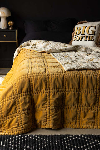 The Reversible Gold Rock & Rose Throw styled on a bed with black bedding and cushions.