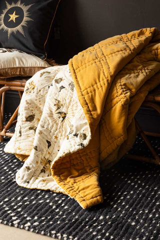 The Reversible Gold Rock & Rose Throw styled draped on a wicker bench.