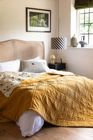 The Reversible Gold Rock & Rose Throw styled on a bed by a window.