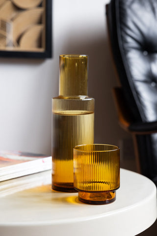 The Ribbed Amber Glass Carafe styled on a table with the matching tumbler next to each other