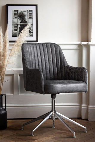 The Ribbed Antique-Style Black Leather Swivel Chair styled in a living room in front of a panelled wall, with an art print and some dried grasses in a vase on the floor.