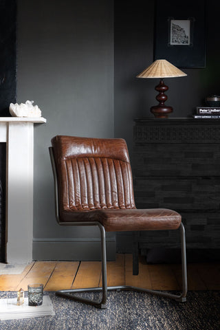 The Ribbed Antique-Style Brown Leather Chair styled on a rug in front of a fireplace and a sideboard, styled with various home accessories.