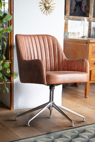 The Ribbed Antique-Style Brown Leather Swivel Chair styled in front of a wall with various furniture, accessories and a plant.