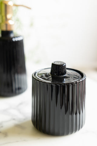 The Ribbed Black Glass Storage Canister styled on a white marble surface with the matching soap dispenser bottle in the background.