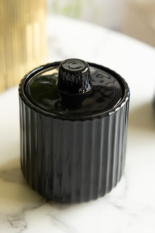 Close-up of the Ribbed Black Glass Storage Canister on a white marble surface.