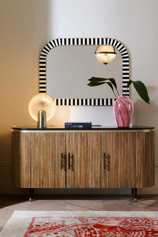 The Ribbed Sideboard styled with a lamp, vase, mirror on the wall and a rug on the floor in front.