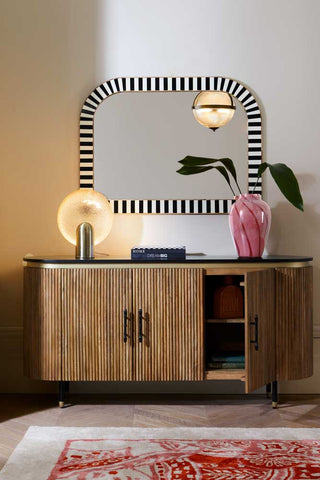 The Ribbed Sideboard styled with a vase, lamp, mirror and rug.