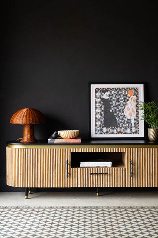 The Ribbed TV Unit in front of a black wall, styled with an art print, lamp, plant, books/magazines, ornament and bowl