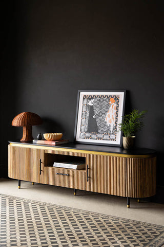 The Ribbed TV Unit styled in front of a dark wall, with an art print, plant, lamp and various other home accessories styled on top.