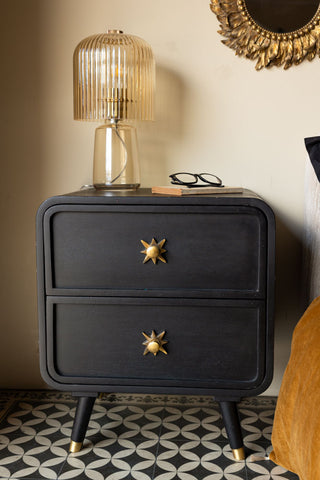 The Ringo Bedside Table styled in front of a neutral wall next to a bed, with a table lamp, book and some glasses on.