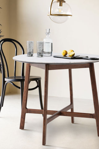 The Round Acacia & Marble Dining Table with kitchen accessories on, styled with a dining chair, overhead light and a plant.