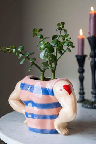 Sailor-themed ceramic storage pot with striped blue and peach design, featuring muscular arms and a heart tattoo, holding a leafy green plant.