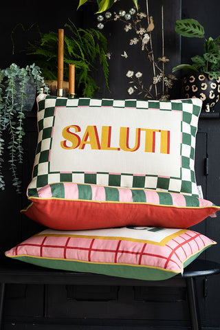 The Saluti Cushion on a stack of cushions, displayed on a bench in front of a black sideboard.