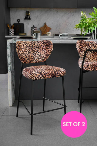 Two leopard print velvet bar stools under a kitchen island. In the background are mugs, jars and serving boards.