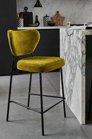 One of the Set Of 2 Bar Stools in Needlecord Velvet Green styled in a kitchen next to a breakfast bar.