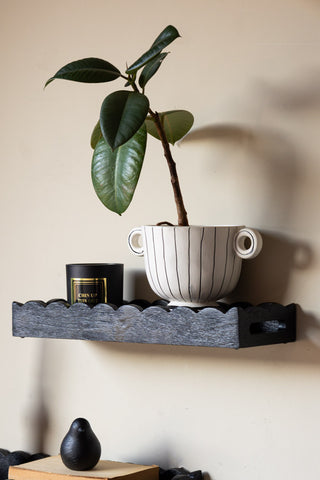 Close-up of one of the Set Of 2 Black Wooden Scalloped Wall Shelves, styled with a candle and plant on.