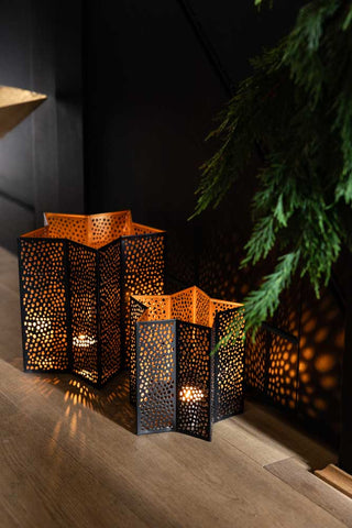 Lifestyle image of the Set Of 2 Black & Gold Star Lanterns along a floor