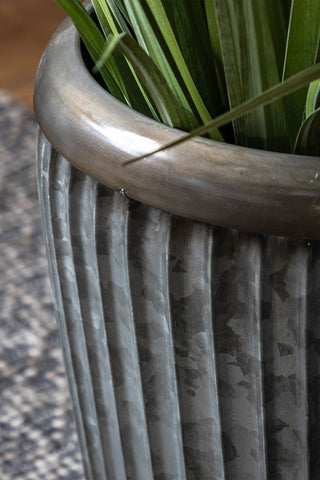 Detail shot of the edge of one of the Set Of 2 Galvanised Iron Ribbed Planters, styled outdoors with a plant inside.