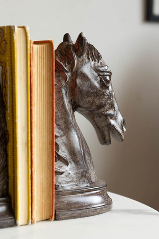 The Set Of 2 Horse Head Bookends displayed on a table with some books inside.