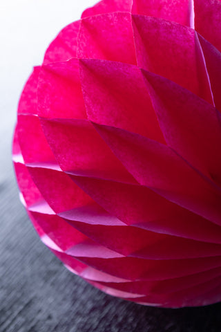 Close-up of one of the Set Of 2 Hot Pink Honeycomb Balls styled on a dark wooden surface.