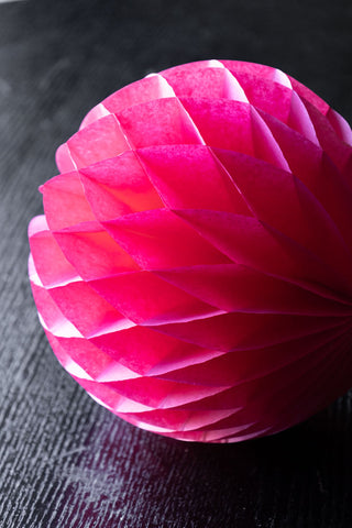 One of the Set Of 2 Hot Pink Honeycomb Balls displayed on a dark wooden surface.