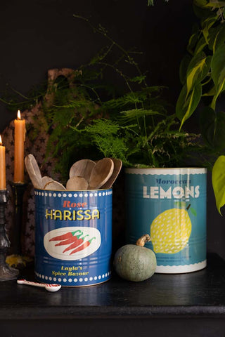 A lifestyle image of The Set Of 2 Lemon & Harissa Storage Tins - Large displayed on a black sideboard, styled with autumnal kitchen accessories