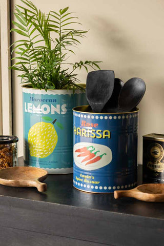 The Set Of 2 Lemon & Harissa Storage Tins - Large displayed on a black sideboard, styled with kitchen accessories and a plant.