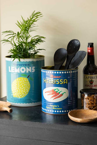 The Set Of 2 Lemon & Harissa Storage Tins - Large displayed together on a black sideboard, styled with kitchen accessories and a plant.