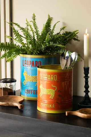 The Set Of 2 Leopard Storage Tins - Large & Medium styled on a black sideboard with a plant and various home accessories.