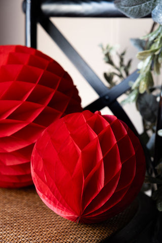 Close-up of the smaller of the Set Of 2 Red Honeycomb Ball Decorations styled on a black cross-back chair.