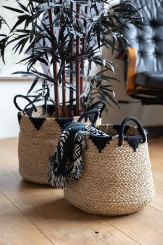 The Set Of 2 Seagrass Baskets displayed on wooden floor with a blanket in the smaller one and a plant in the larger one.