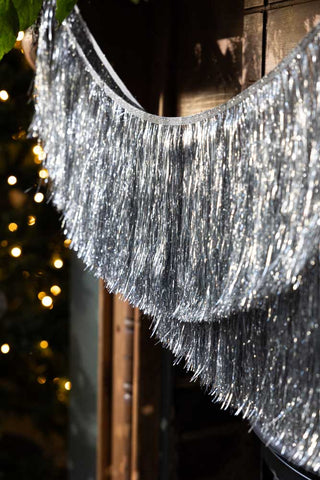 Close-up of the Set Of 2 Silver Tinsel Christmas Garlands hung under a wooden mantlepiece.