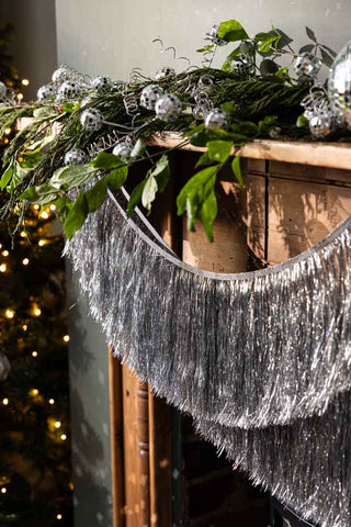 The Set Of 2 Silver Tinsel Christmas Garlands hung under a fireplace.