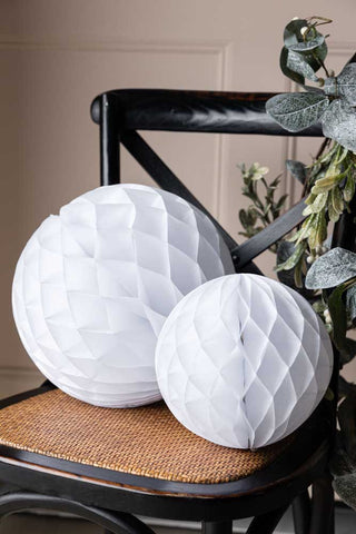 The Set Of 2 White Honeycomb Ball Decorations styled next to a green leaf garland on a brown and black chair.