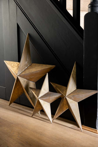 Lifestyle image of the Set Of 3 Antique Gold Metal Stars leaning against a wall