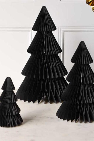 A lifestyle image of the Set Of 3 Black Honeycomb Christmas Trees in a white table with gold paper fans on the wall