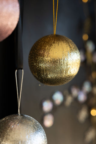 Close-up of the gold bauble in the Set Of 3 Metallic Spun Thread Christmas Bauble Decorations, with the others also in shot, in front of a dark wall styled with decorations and fairy lights.