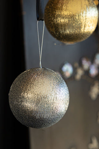 Close-up of the silver and gold baubles from the Set Of 3 Metallic Spun Thread Christmas Bauble Decorations, hanging in front of a dark wall.