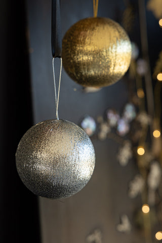 Detail shot of the silver and gold baubles from the Set Of 3 Metallic Spun Thread Christmas Bauble Decorations, hanging in front of a black wall with fairy lights.