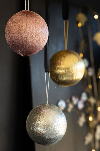 The Set Of 3 Metallic Spun Thread Christmas Bauble Decorations hanging in front of a dark wall, with decorations and fairy lights in the background.