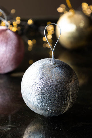 The Set Of 3 Metallic Spun Thread Christmas Bauble Decorations, with the silver at the front, styled on a dark surface with fairy lights.