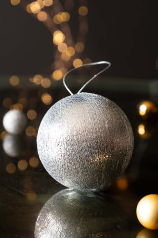 The Silver Metallic Spun Thread Christmas Bauble Decoration styled on a black surface with small baubles and fairy lights.